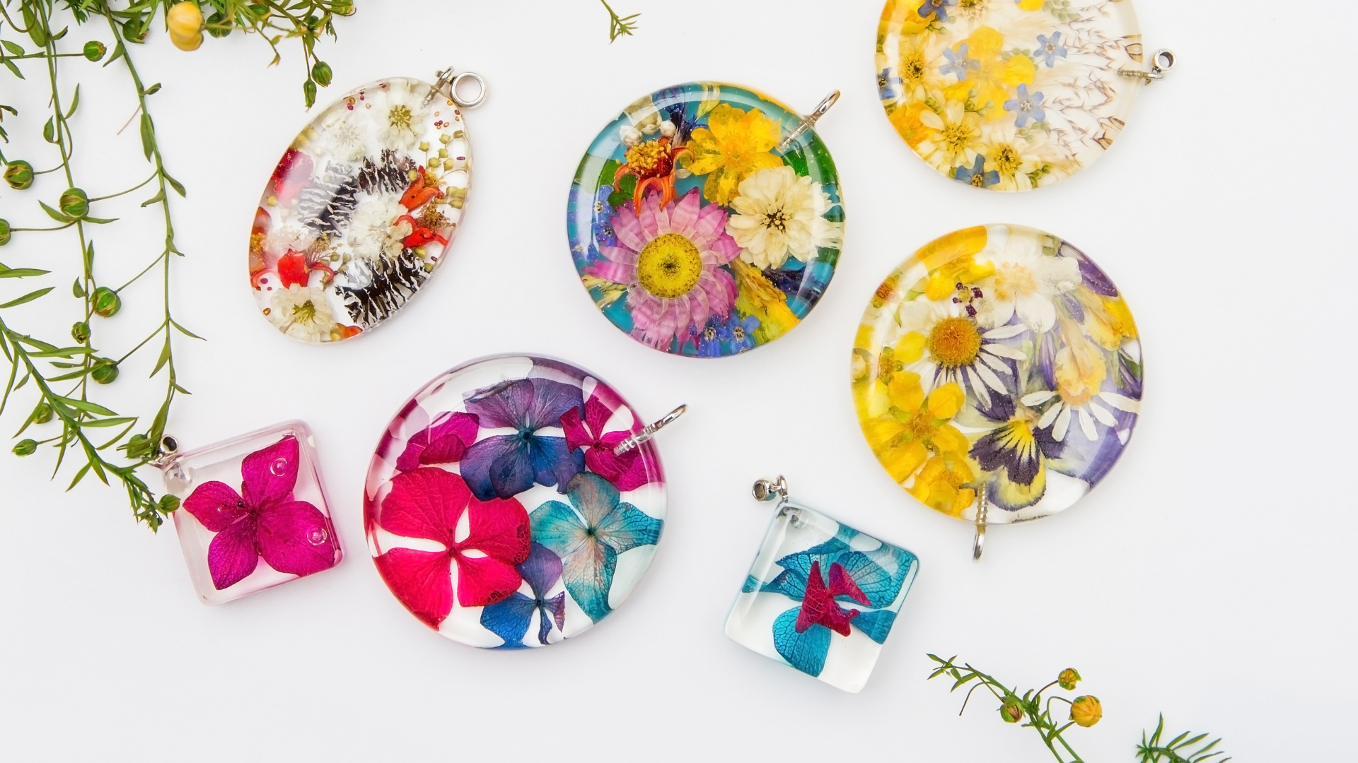 Four pieces of resin jewelry bright with dried flowers and decorative plants on a white background.