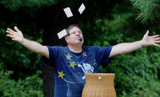 Ed Popielarczyk, a white man, stands with his arms outstretched and eyes closed as playing cards flutter in the air around him