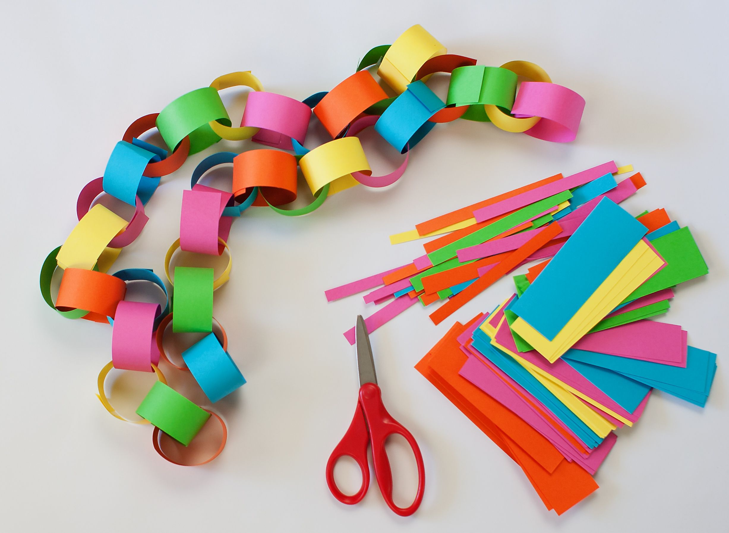 A multicolored paper chain lying next to scissors and strips of paper.